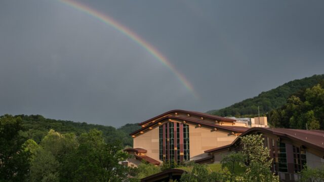 A rainbow in a dark grey sky over a tribal casino building in the mountains