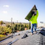 Man carrying a solar panel on a roof in Southern California.