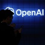 Visitor look at their phone next to an Open AI's logo during the Mobile World Congress (MWC), the telecom industry's biggest annual gathering, in Barcelona on February 26, 2024. The world's biggest mobile phone fair throws open its doors in Barcelona with the sector looking to artificial intelligence to try and reverse declining sales. (Photo by PAU BARRENA/AFP via Getty Images)