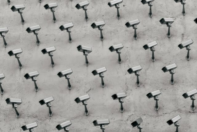 a pattern of CCTV surveillance cameras on a wall, all pointing in different directions.