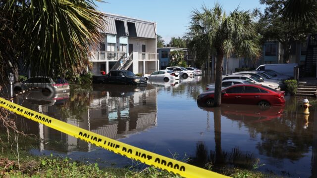 Yellow police tape is draped in front of a parking lot in which cars sit in several feet of water