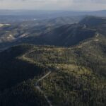 An aerial shot of a green forest running along a mountain ridge with a road in the middle