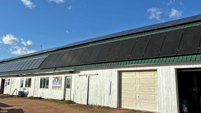 a wide white outbuilding on a farm with many solar panels on the roof