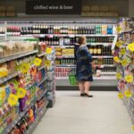 A customer holds a shopping basket as she browses the wine and beer section inside a Morrisons M Local store