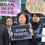 A small group of protesters hold signs, mostly in Korean, but one reads