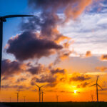 Wind turbines stand against a sunset near the Gulf of Mexico.