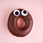 Close-up of a surprised doughnut with chocolate icing and googly eyes.