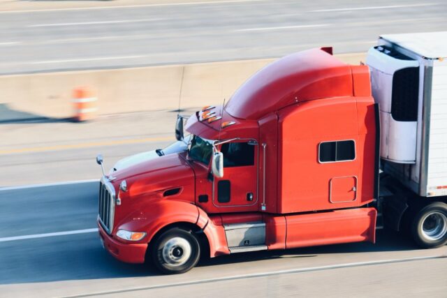 A red semi towing a trailer drives down a highway.