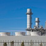 Smoke stacks from a natural gas power plant stand against a blue sky.