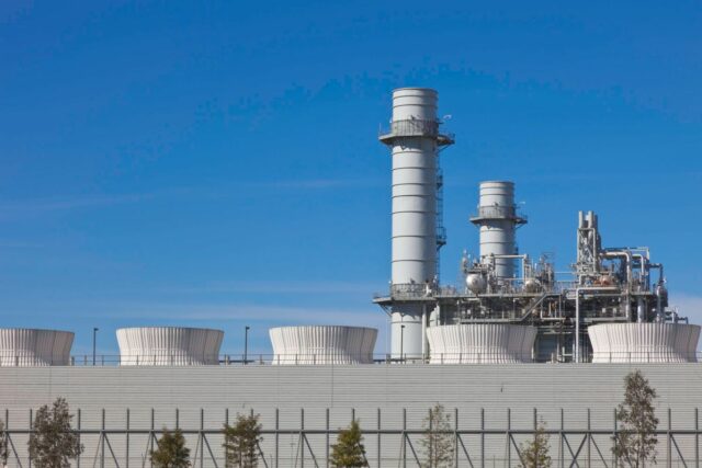 Smoke stacks from a natural gas power plant stand against a blue sky.