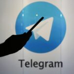 Telegram logo behind silhouette of person checking a mobile device