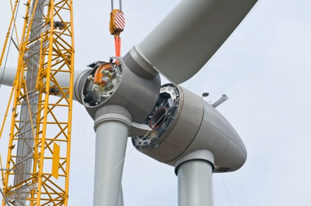 A crane positions the rotor of a wind turbine during construction.