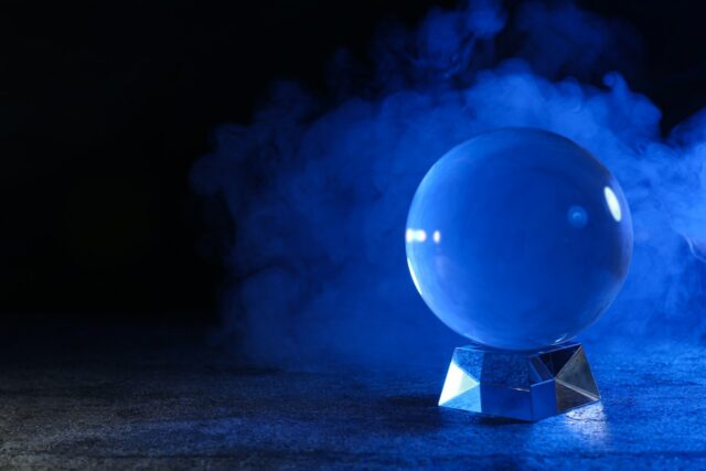 Magic crystal ball on table and smoke against dark background, space for text. Making predictions