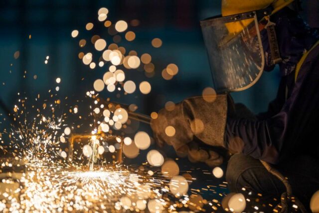 A metalworker cuts steel in a workshop.