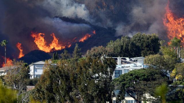 Photo of flames erupting into a dark sky behind homes on a hillside