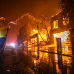 A firefighter battles the Palisades Fire while it burns homes at Pacific Coast Highway amid a powerful windstorm on January 8, 2025 in Los Angeles, California.