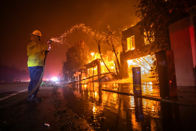 A firefighter battles the Palisades Fire while it burns homes at Pacific Coast Highway amid a powerful windstorm on January 8, 2025 in Los Angeles, California.