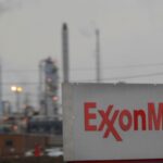 Exxon Mobil sign in foreground with smokestacks of a petrochemical factory in background