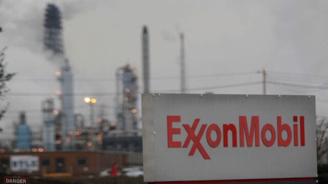 Exxon Mobil sign in foreground with smokestacks of a petrochemical factory in background