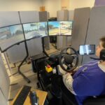 A Vay teleoperator in Las Vegas sits behind a steering wheel viewing 3 large monitors.