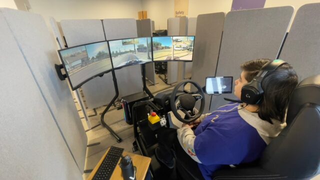 A Vay teleoperator in Las Vegas sits behind a steering wheel viewing 3 large monitors.