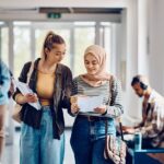 Two female university students walking down corridor.