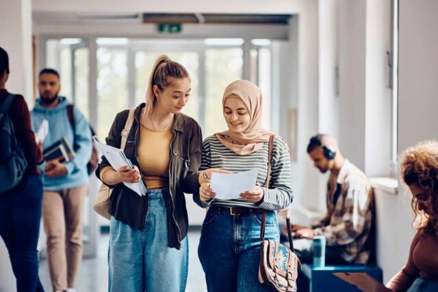 Two female university students walking down corridor.