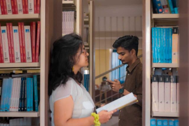 Two students in-between bookshelves in a library.